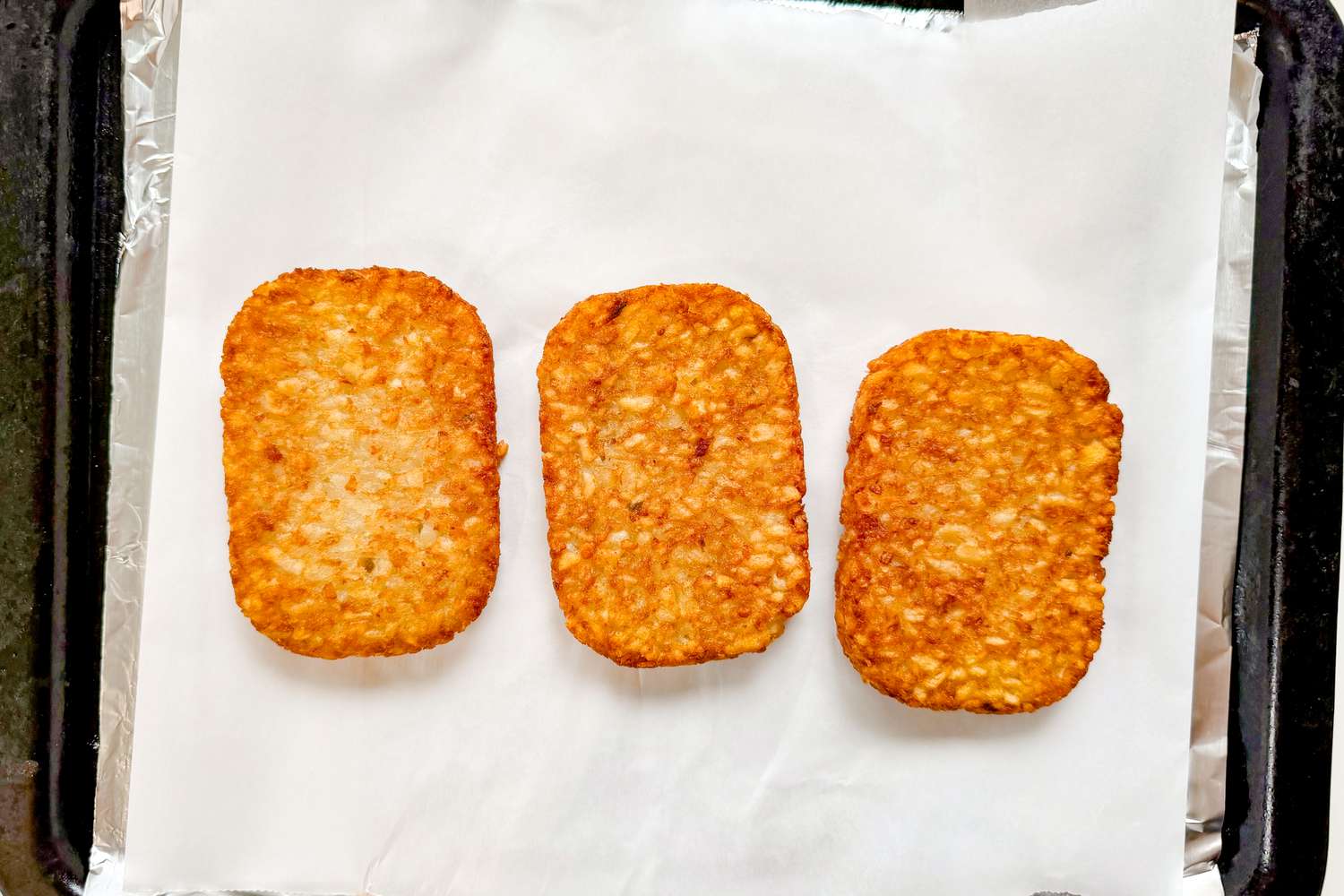 Three hash brown patties arranged in a row on a parchmentlined baking sheet