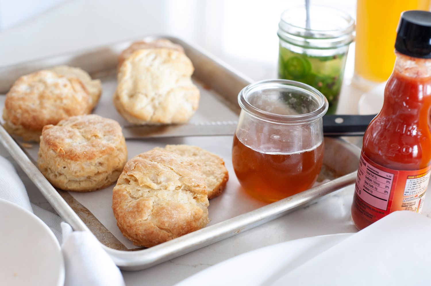 Biscuits on a sheet pan with honey, hot sauce, and pickles