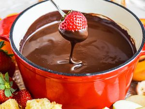 Dipping a strawberry into fondue chocolate with other dippers surrounding.
