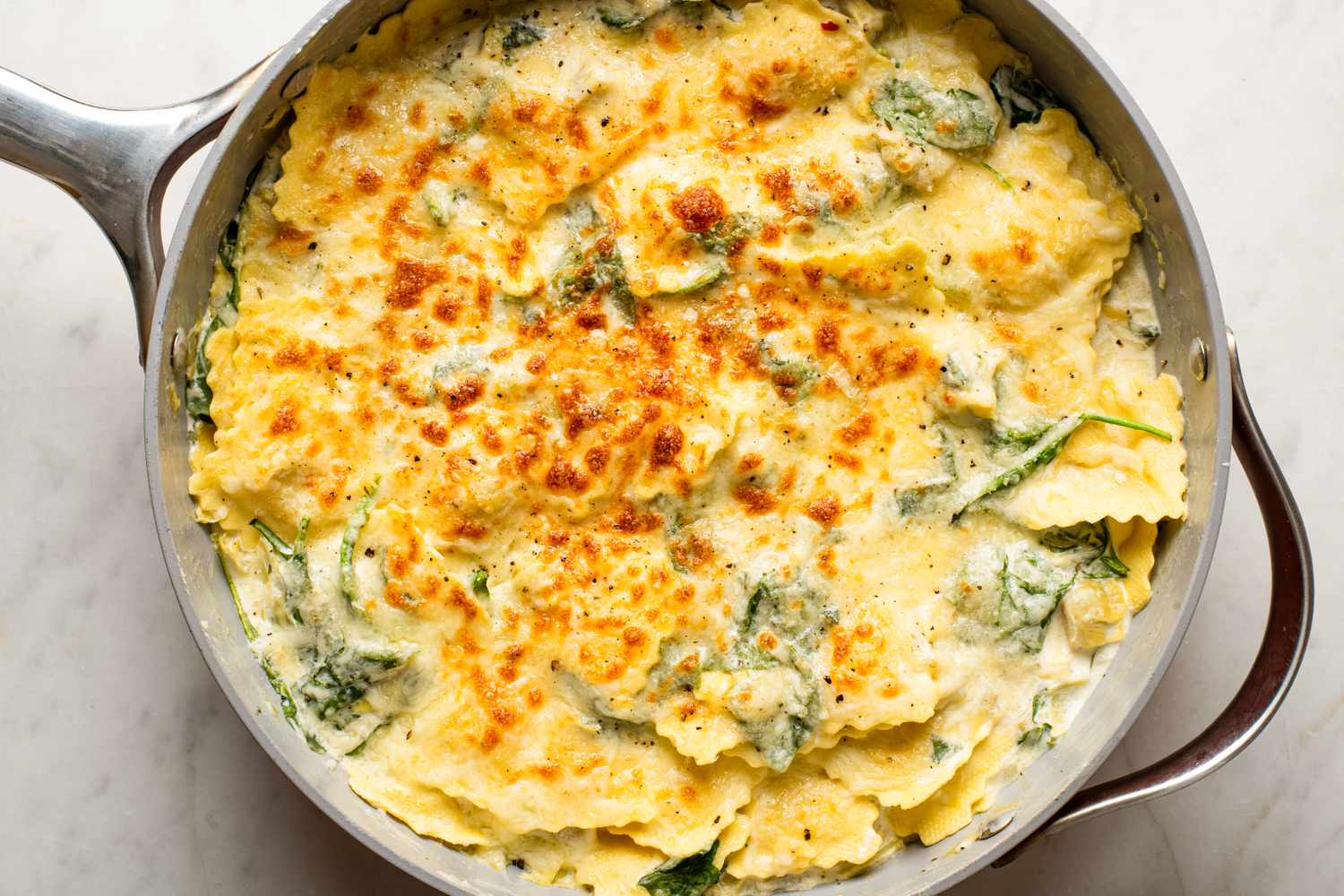Baked spinach artichoke ravioli in a skillet topped with melted cheese