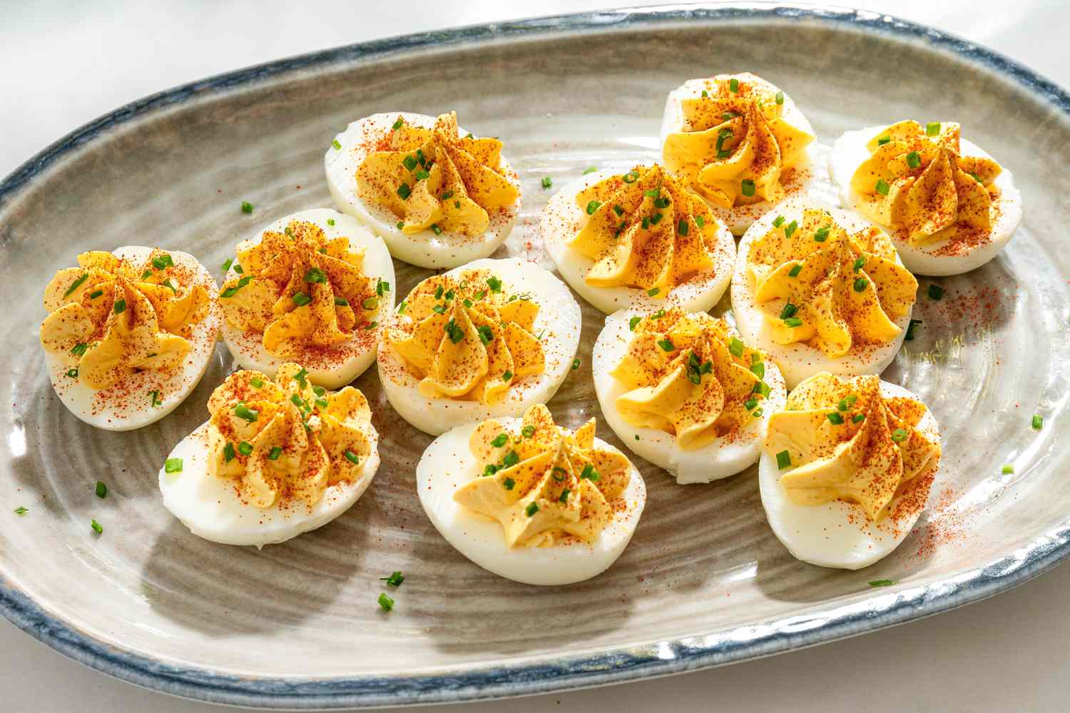 A ceramic serving plate with million dollar deviled eggs, garnished with chopped chives and paprika
