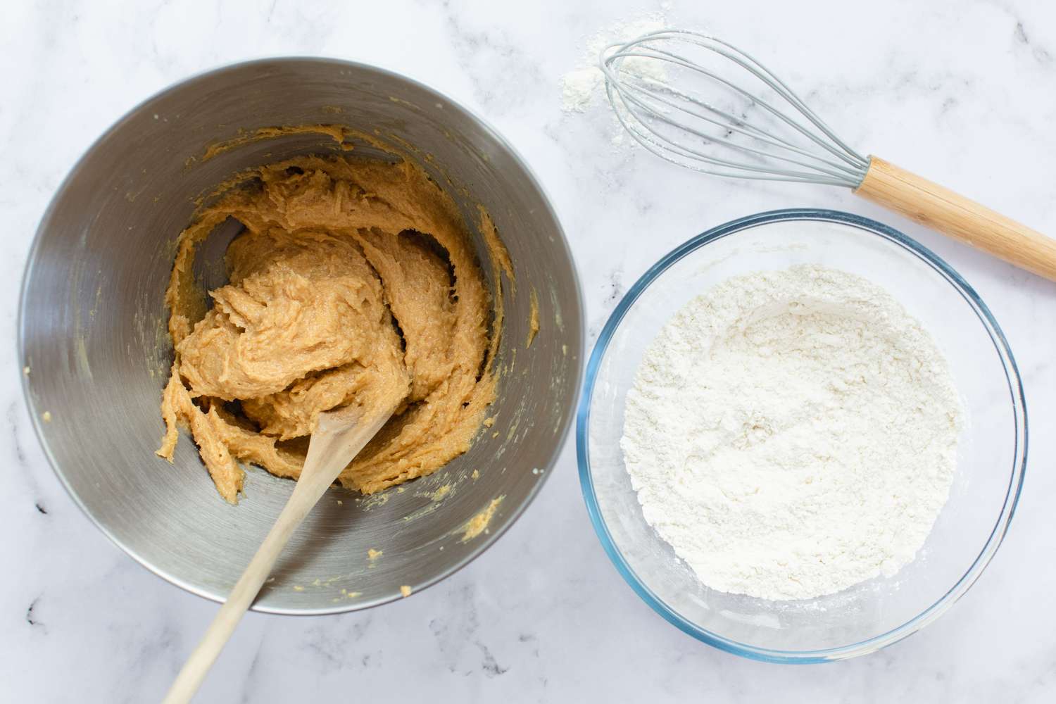 Peanut butter in a metal bowl with flour in a glass bowl next to it.