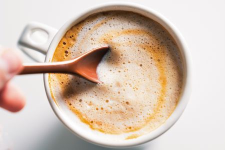 A cup of coffee with milk foam a spoon dipping into the foam