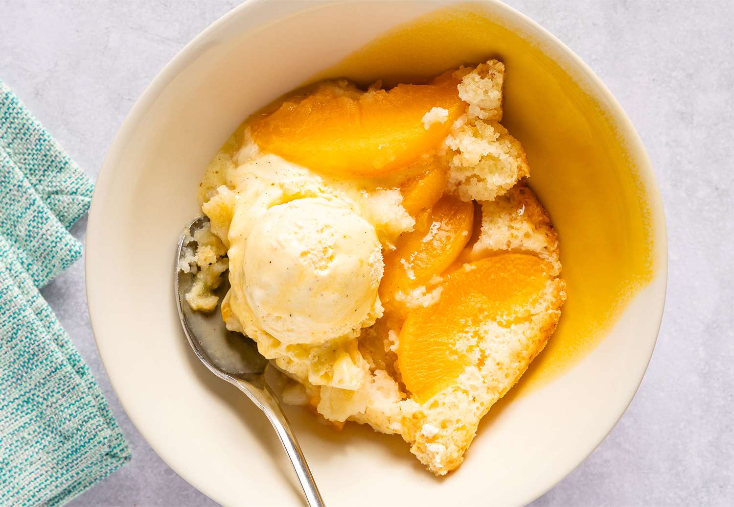 Peach cobbler served with ice cream in a bowl with a spoon