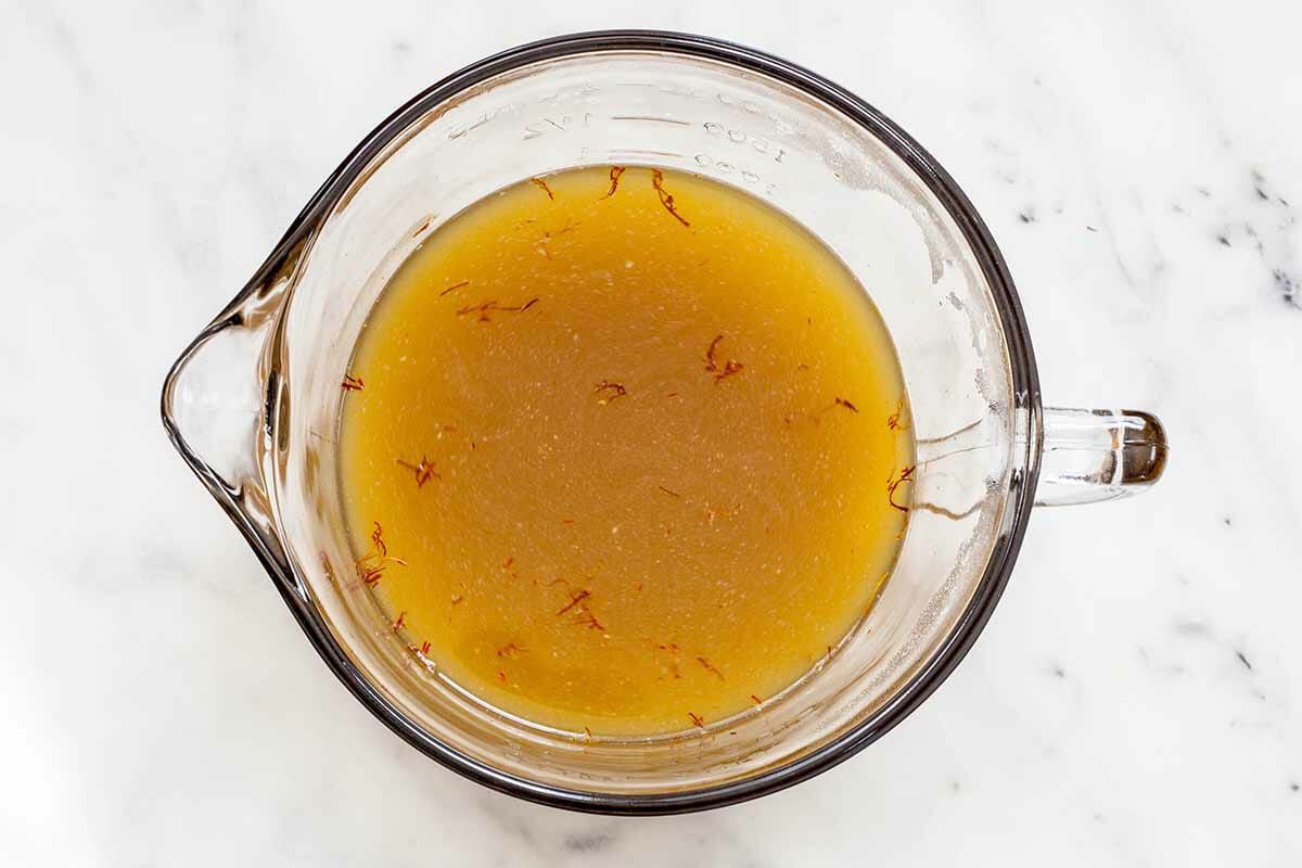 Saffron being steeped in a broth in a measuring glass