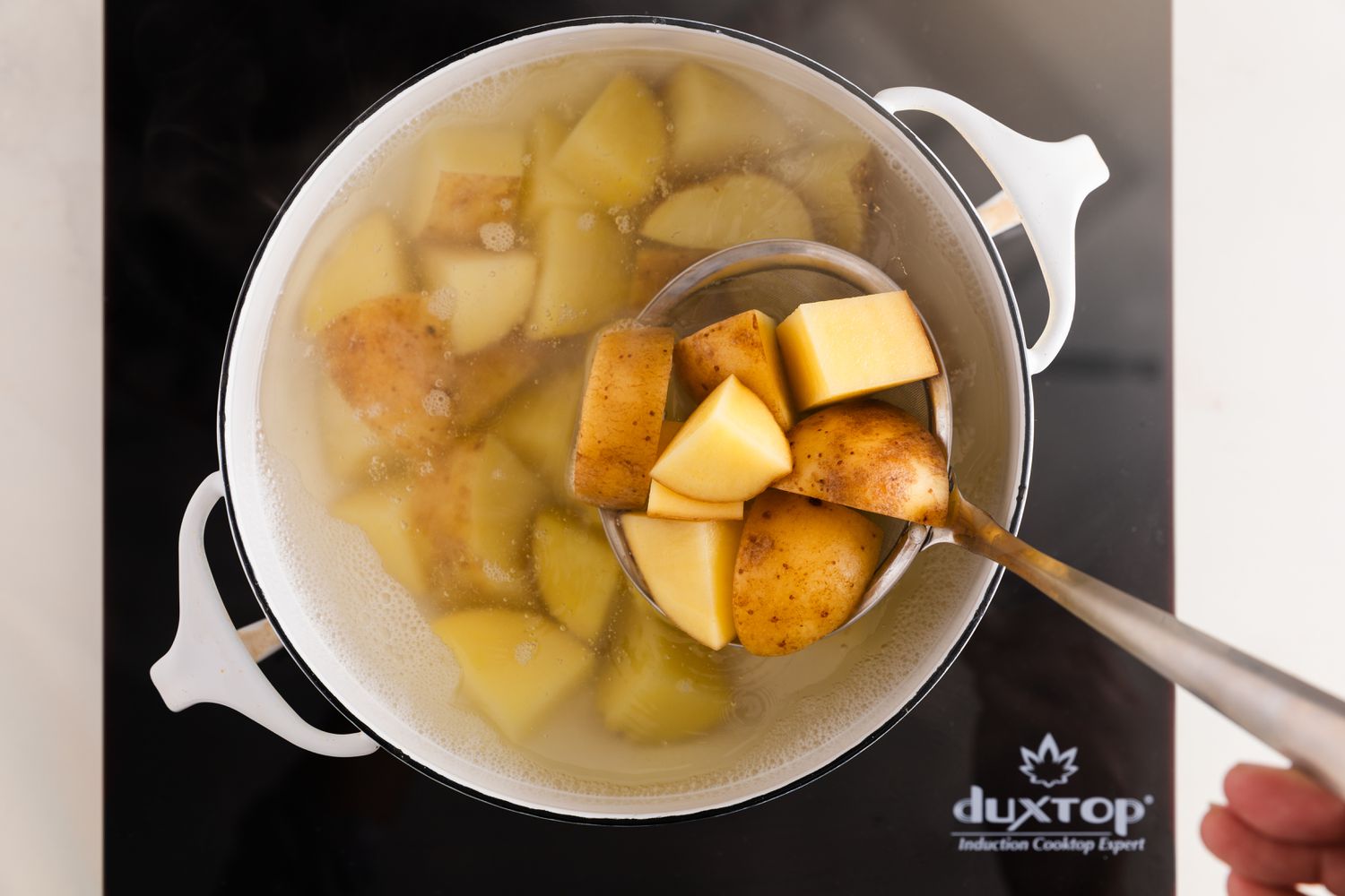 Quartered Potatoes Placed Into a Pot of Boiling Water Using a Mesh Skimmer on an Induction Stove