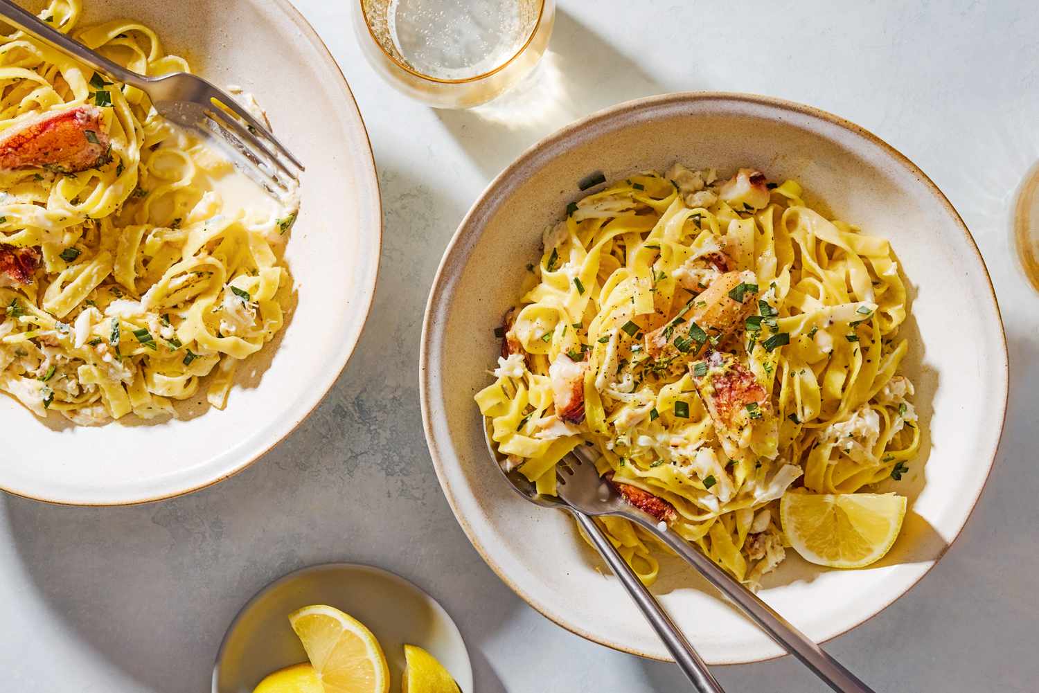 Overhead shot of two bowls with 5-ingredient creamy crab pasta, with a lemon wedge and chopped fresh tarragon as garnish
