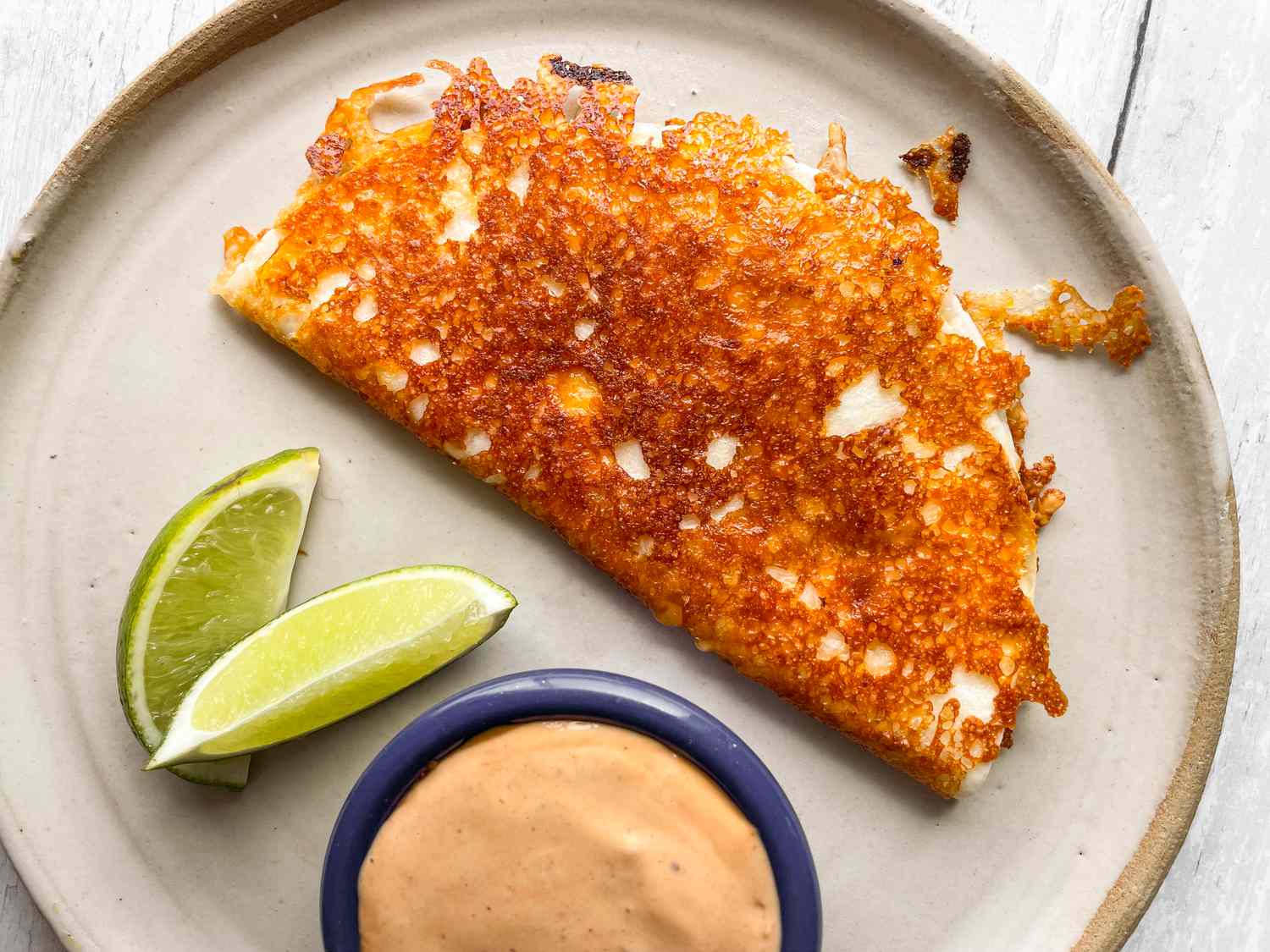 Burnt Cheese Taco on a Plate with Chipotle Sauce and Lime Wedges