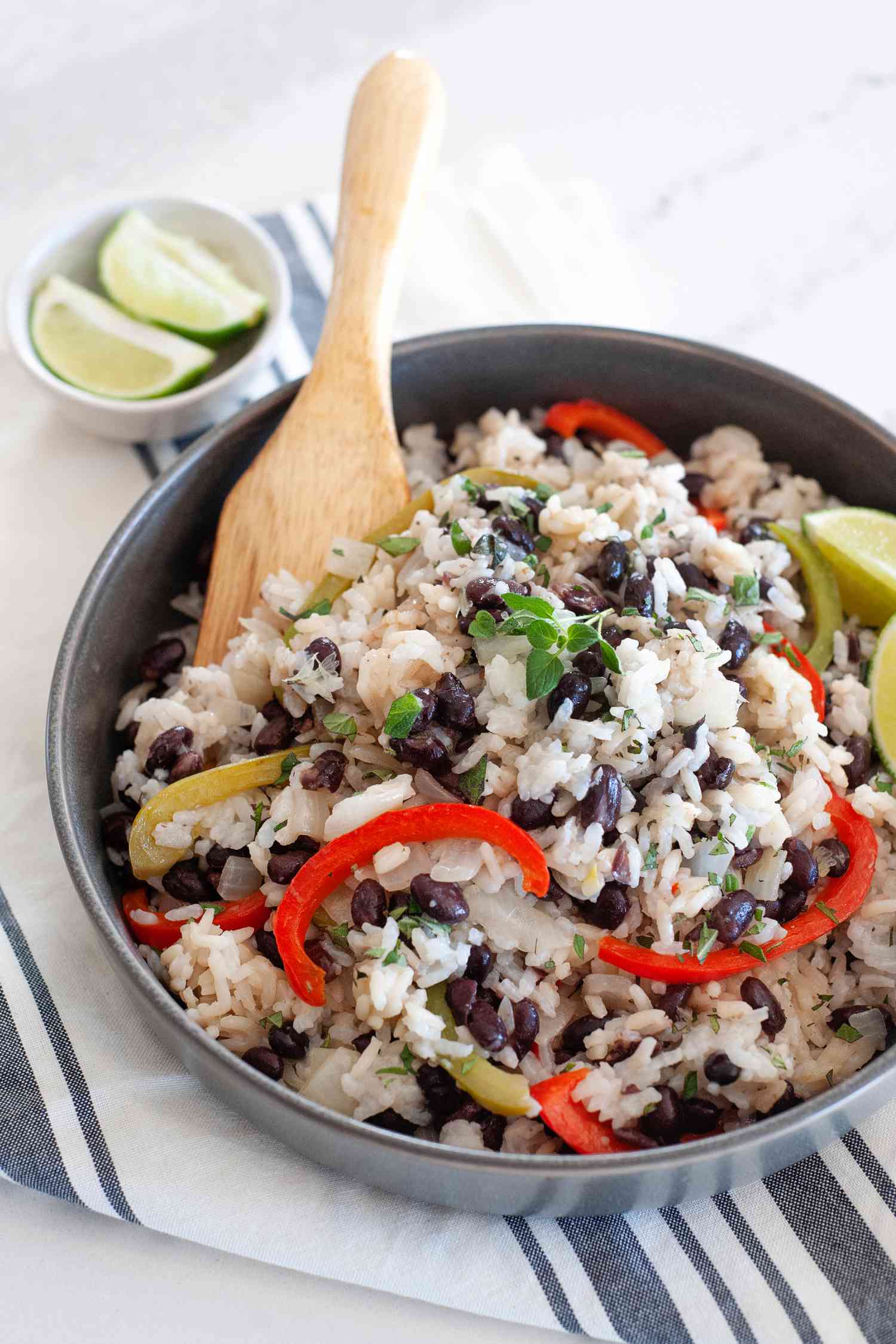 Side view of a bowl of black beans and rice with a wooden spoon and a striped linen.