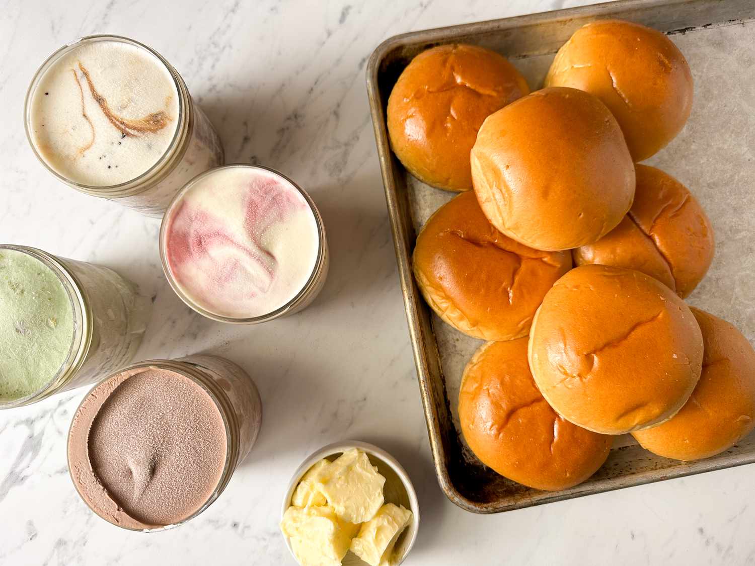 Brioche buns on a tray, jars of various ice creams, and a bowl of chips on a table