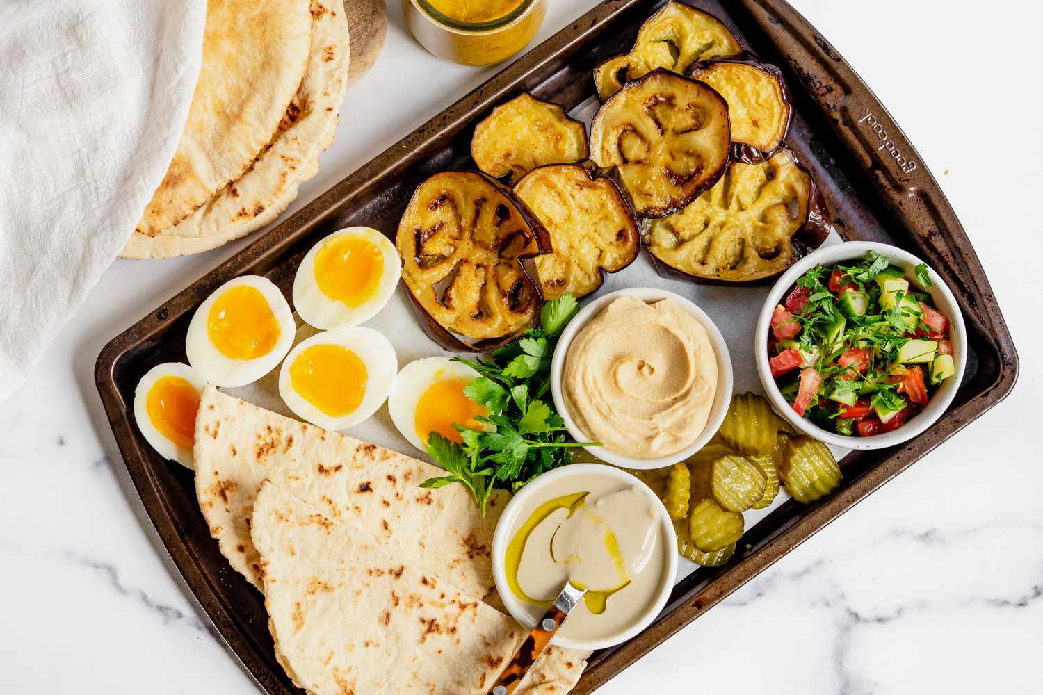 Tray of Ingredients (Fried Eggplant, Boiled Eggs, Bowl of Tahini, Bowl of Israeli Salad, Bowl of Hummus, Pickles, and Pita Bread) for Sabich