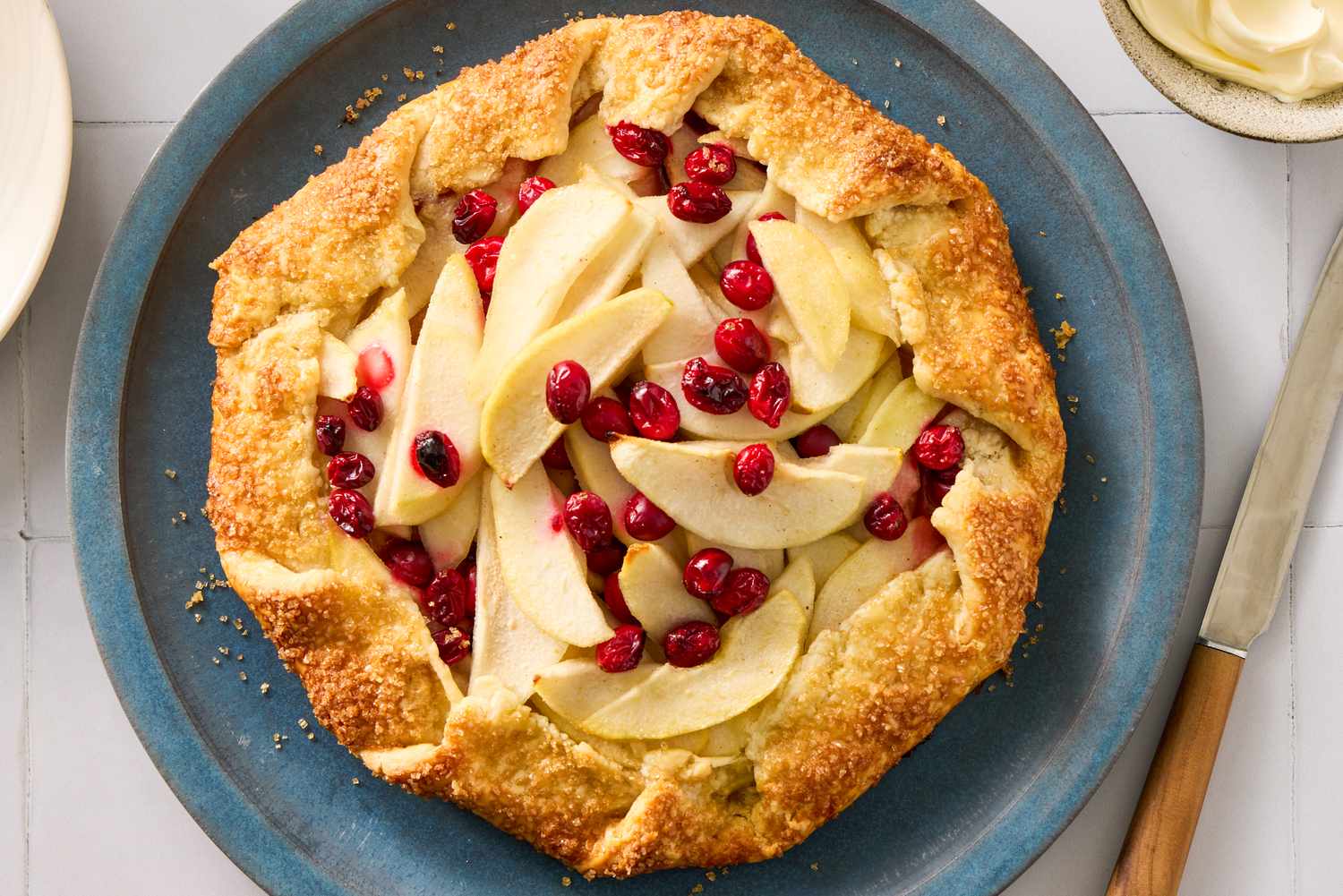 A pear and cranberry galette placed on a plate with a knife nearby
