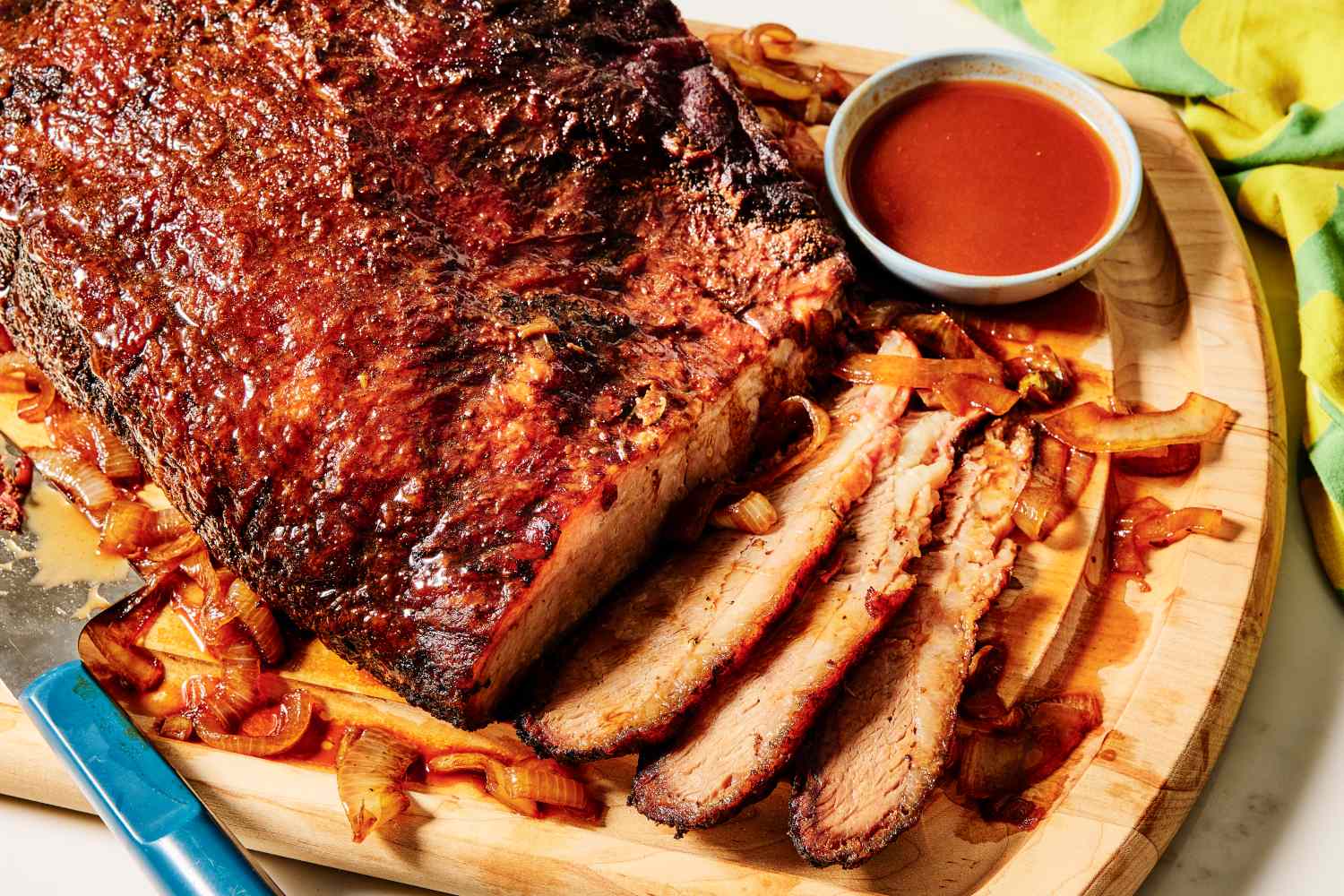 Slowcooked brisket sliced on a wooden cutting board with a bowl of sauce on the side