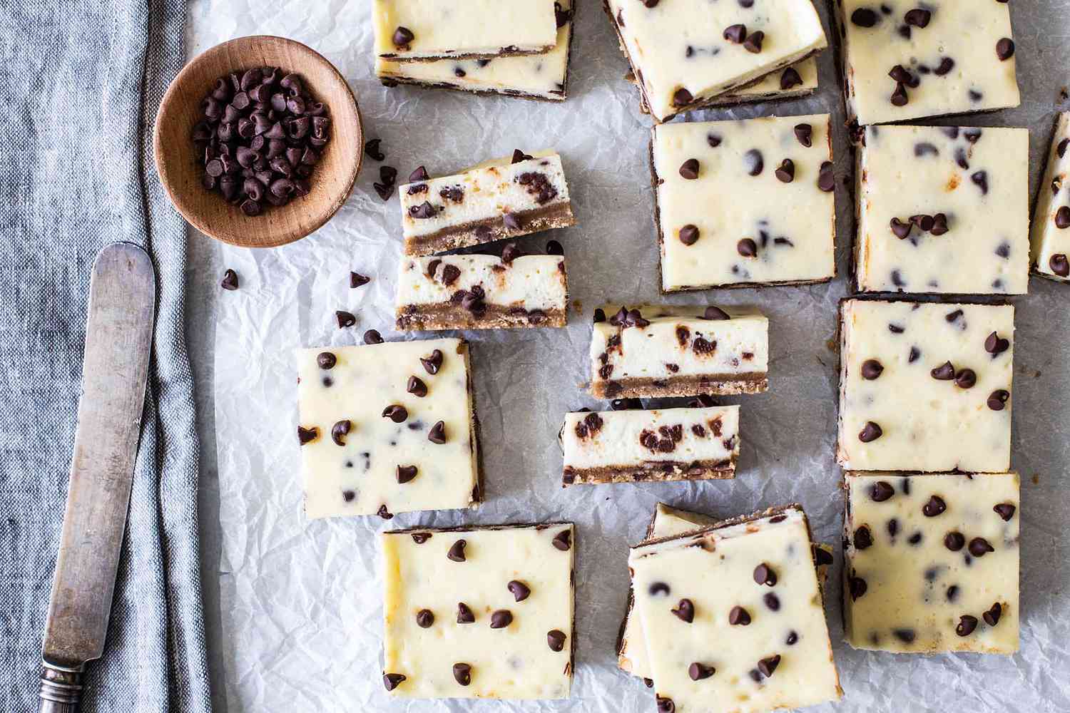 Chocolate chip cheesecake bars on parchment paper with chocolate chips on the side