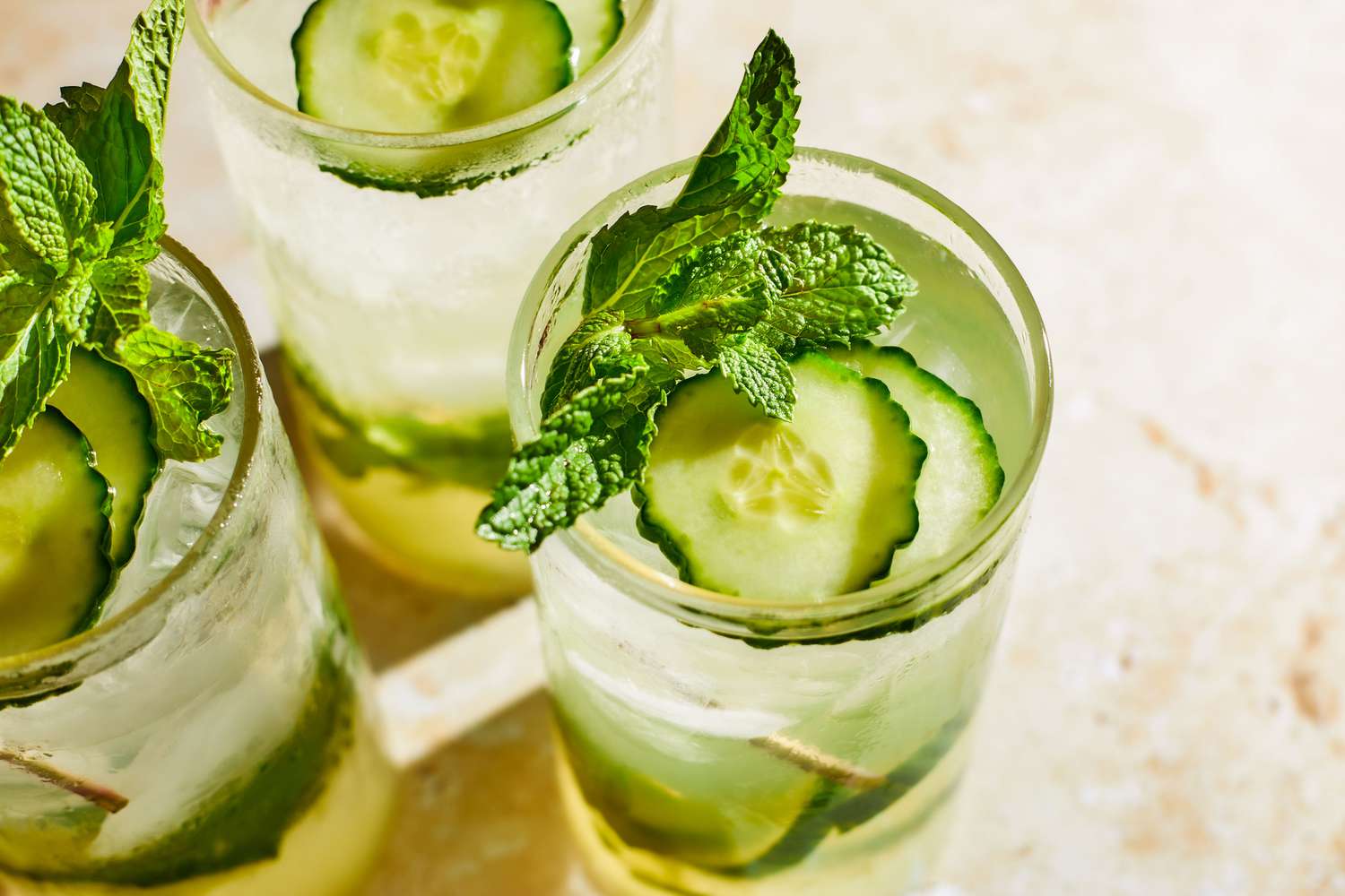 3 cocktail glasses filled with 3-Ingredient Mocktail, garnished with cucumber slices and mint leaves