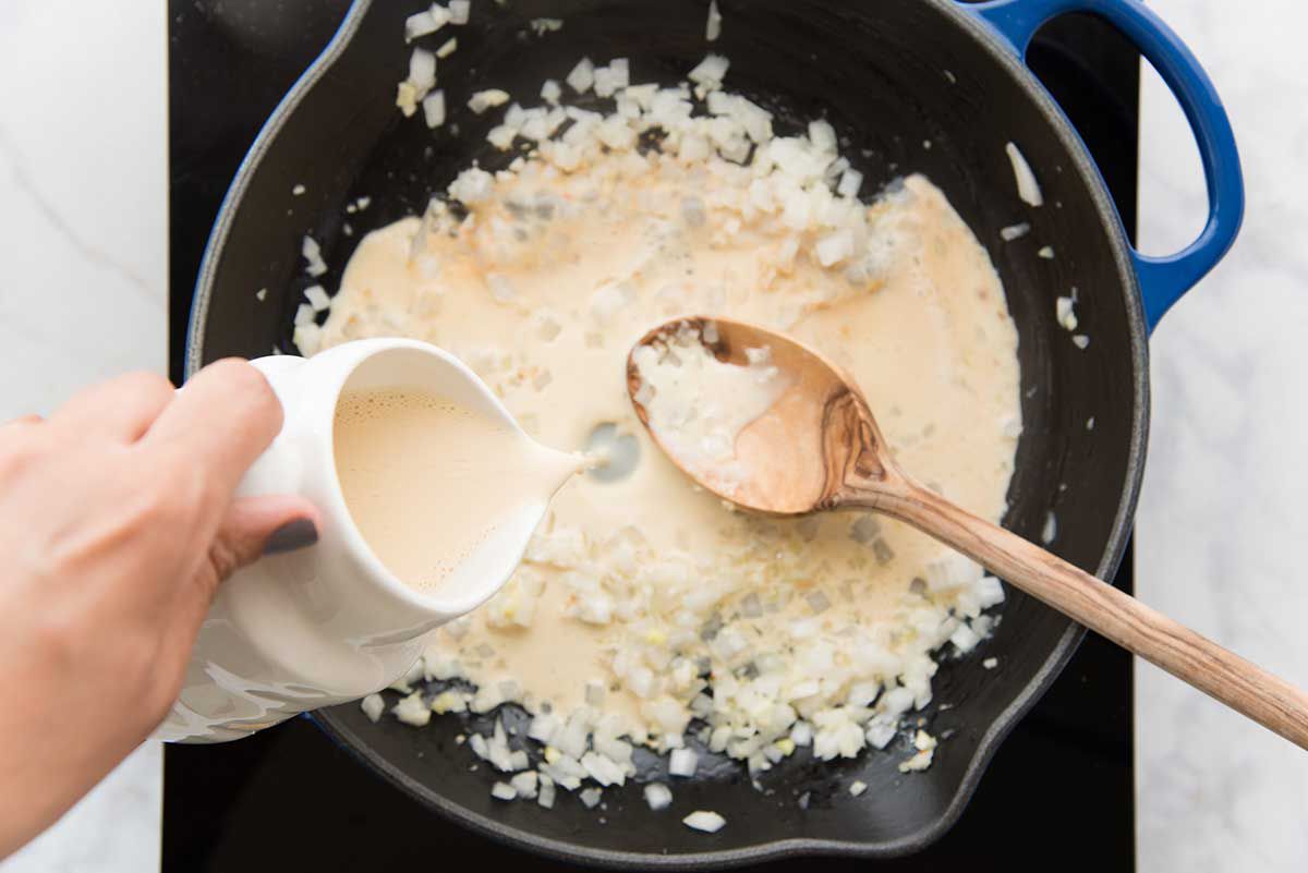 Milk poured into a pan with sauteed onions for homemade queso