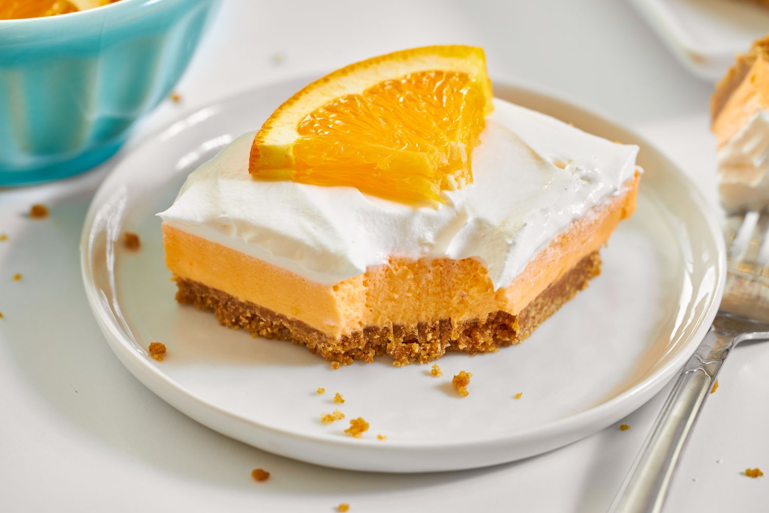 Creamsicle dessert bar with a graham cracker crust orange filling whipped topping and an orange slice garnish on a white plate