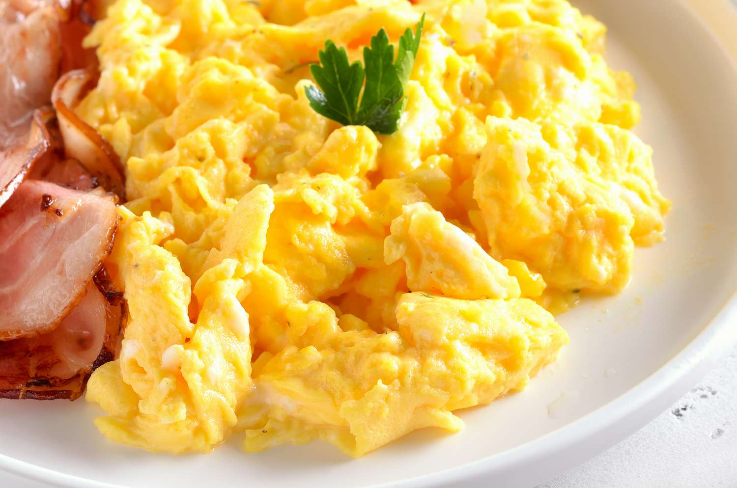 scrambled eggs on a plate with slices of bacon