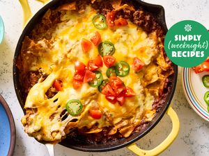 A skillet filled with cheesy nachos topped with diced tomatoes and jalapeos marked with a Simply Weeknight Recipes label