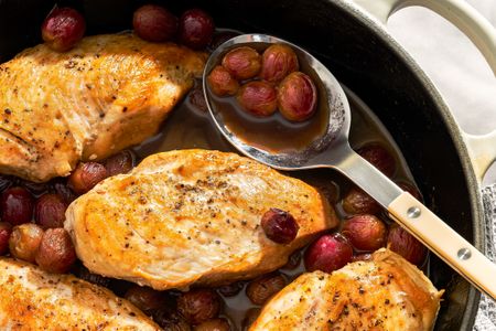 Cooked chicken breasts in a pan with grapes and balsamic sauce a serving spoon holding grapes and sauce