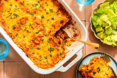 Chicken taco casserole (with a serving cut out) at a table setting with a serving on a plate, glasses, and a side salad