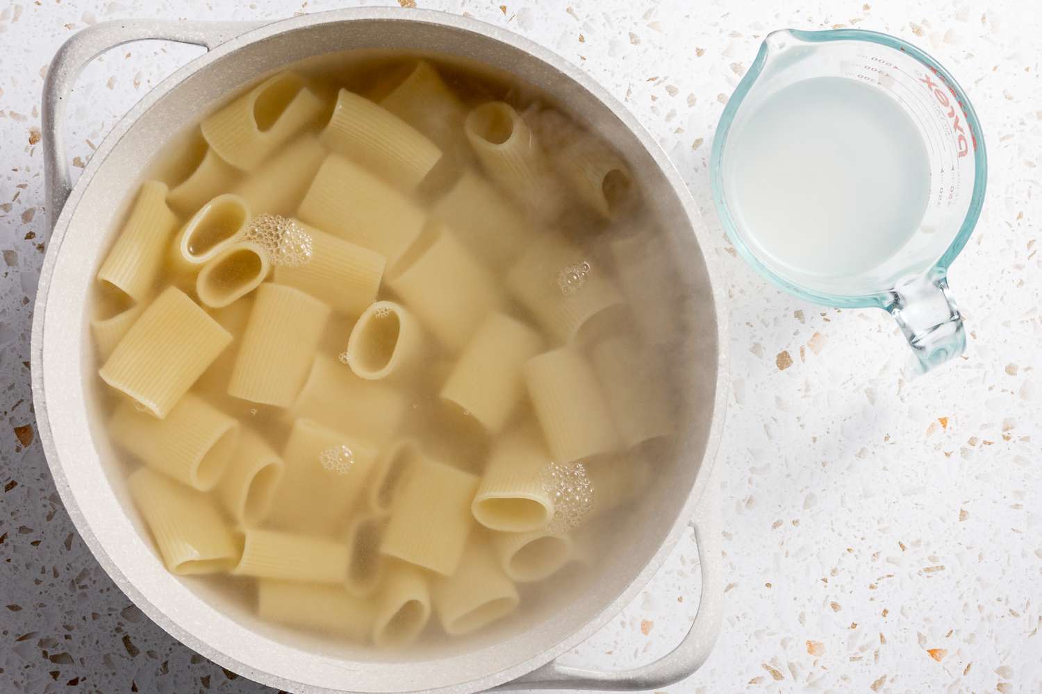 Pasta Water Reserved in a Pyrex Measuring Cup Next to the Pot of Boiling Pasta