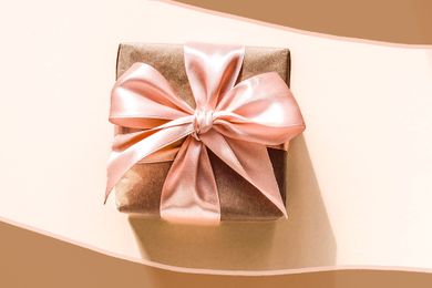 Image: gift wrapped in brown wrapping paper and covered with a pink bow and in the perimeter of image, brown and pink color block illustrations