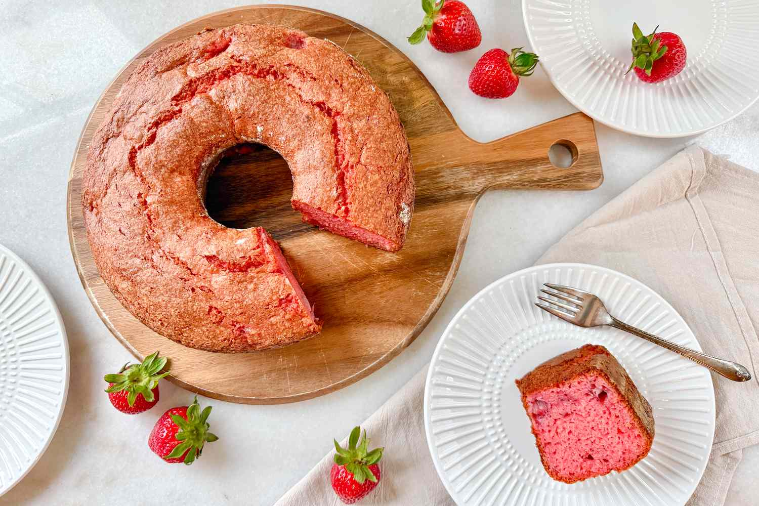Strawberry bundt cake on a wooden tray with a slice served on plates, garnished with strawberries