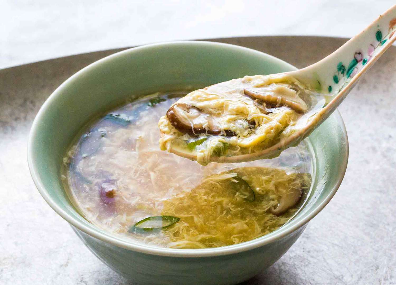 A bowl of egg drop soup with a spoon lifting a mouthful