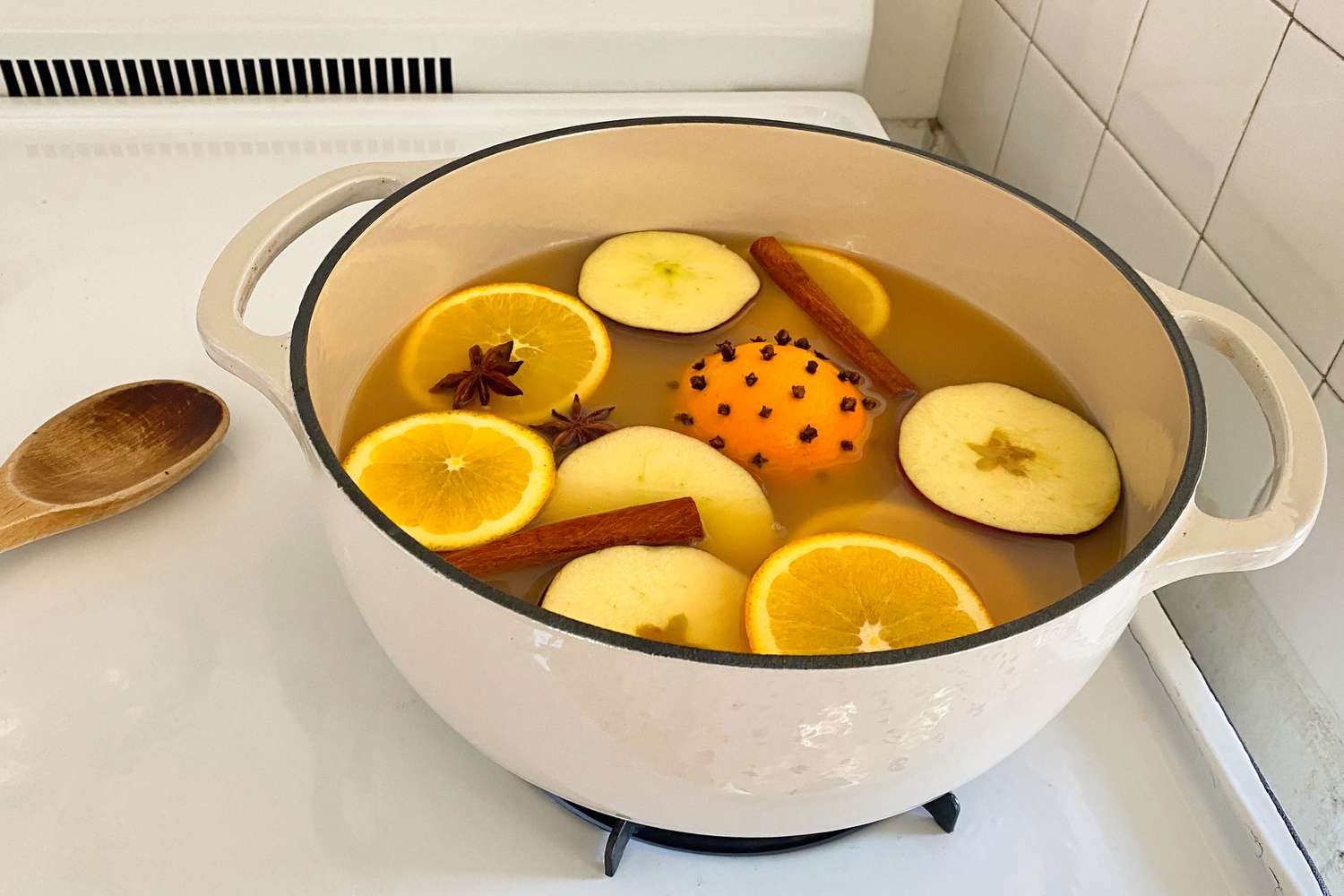 large pot with cider, slices or orange and apple, pomander ball, star anise, and cinnamon sticks on a stove