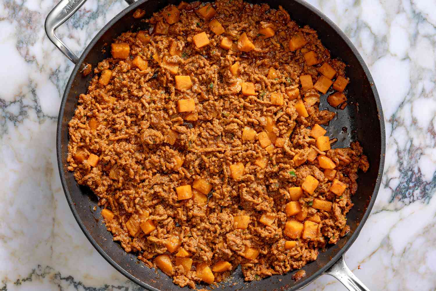Overhead view of a skillet of the ground beef mixture after adding sweet potatoes for Easy Puerto Rican Picadillo recipe