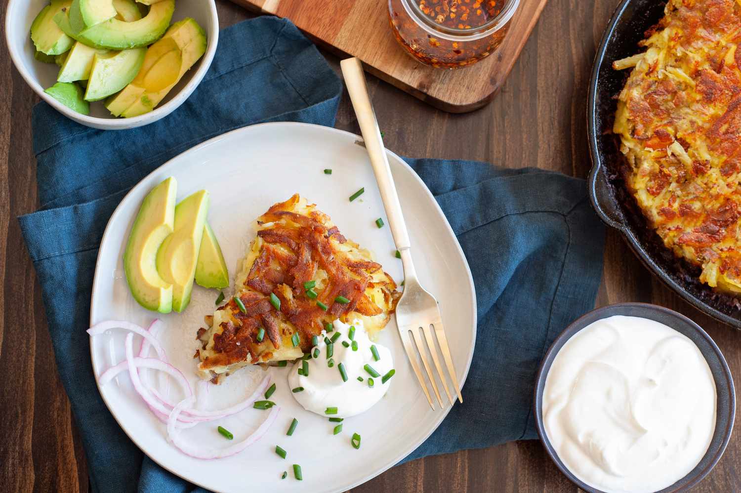 Slice of Rosti on a Plate with Sour Cream, Sliced Avocados, and Sliced Onions