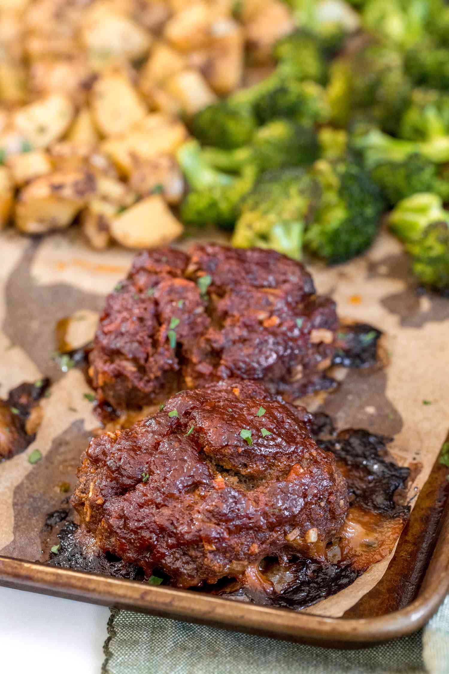 Mini meatloaves with broccoli and potatoes on a sheet pan.