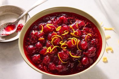 A bowl of cranberry sauce garnished with lemon zest with a spoon in the background
