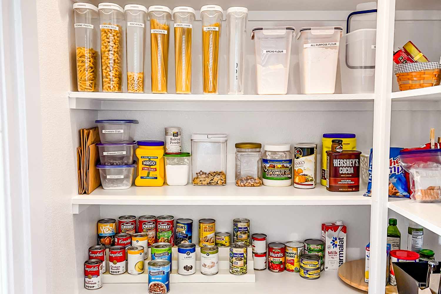 A neatly organized pantry with jars of pasta containers of grains canned goods and various other food items arranged on shelves