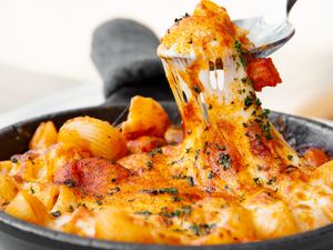 Pasta dish topped with melted cheese being pulled with a fork