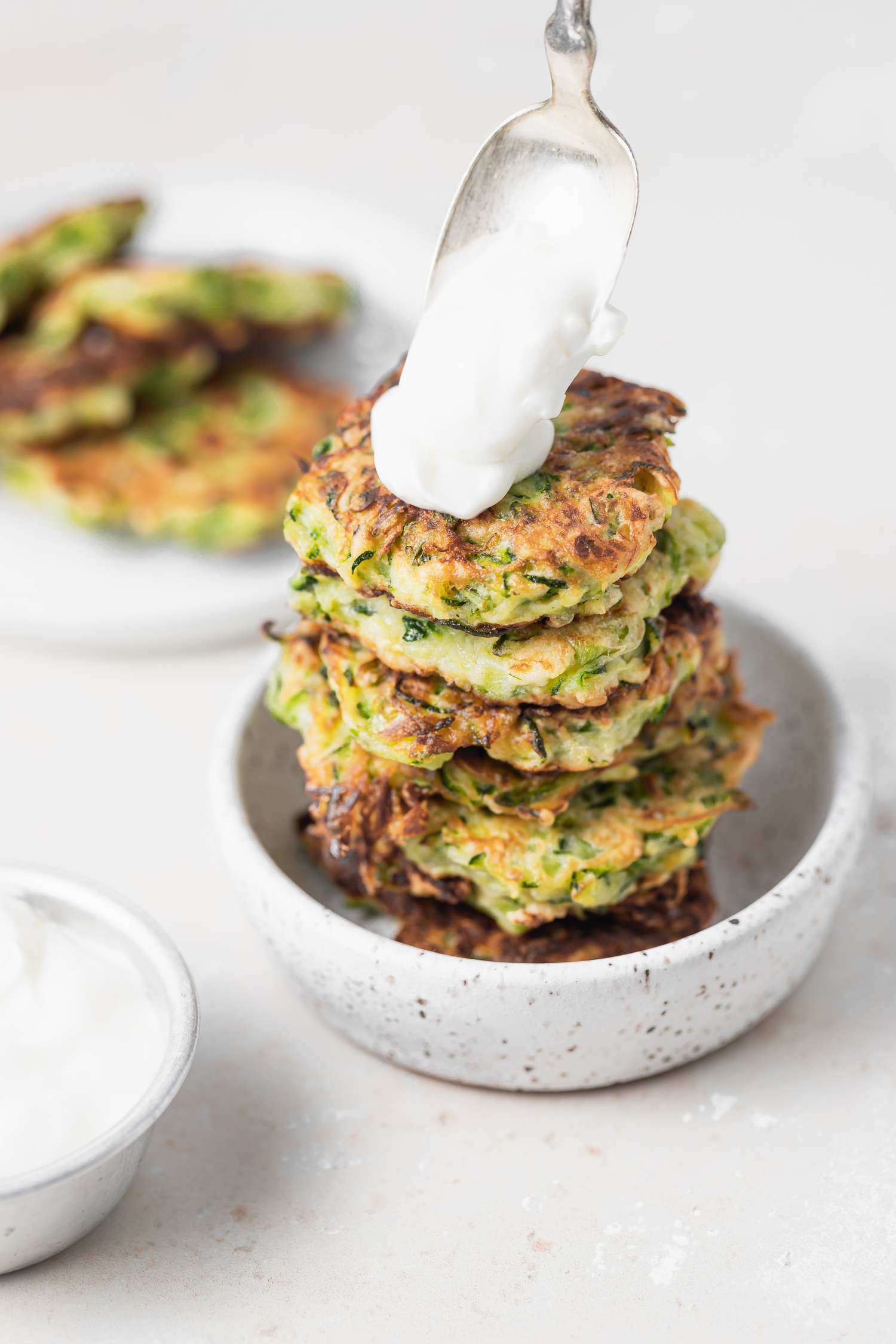 A stack of zucchini fritters being topped with sauce.