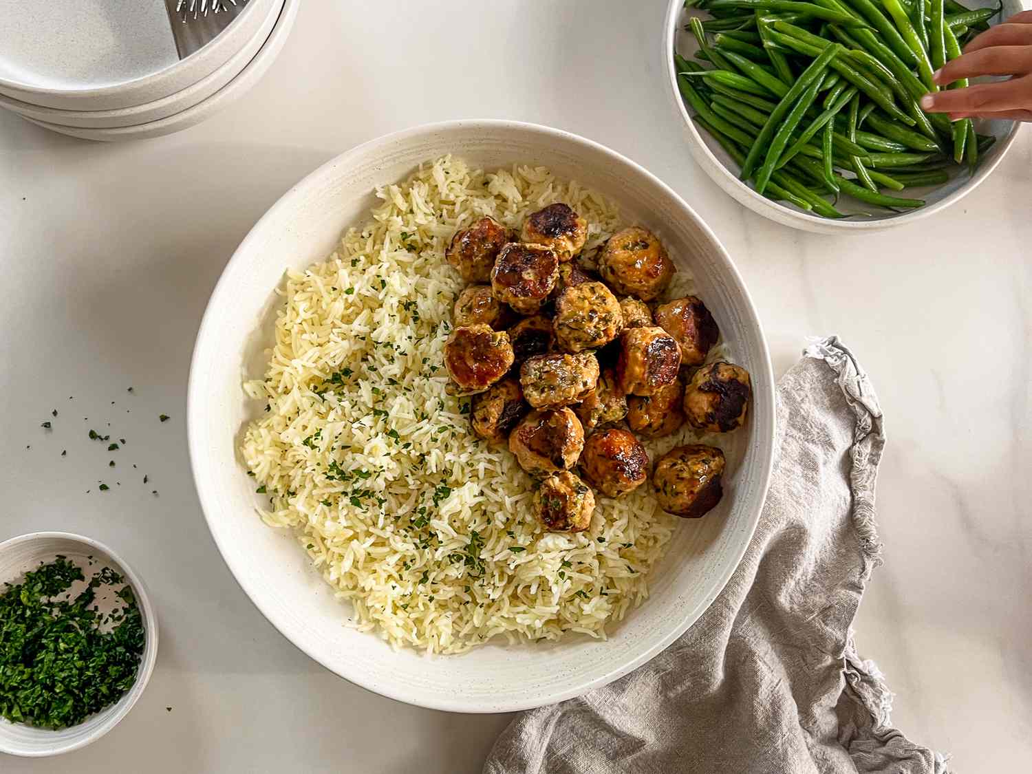 A bowl of rice topped with meatballs alongside a dish of green beans