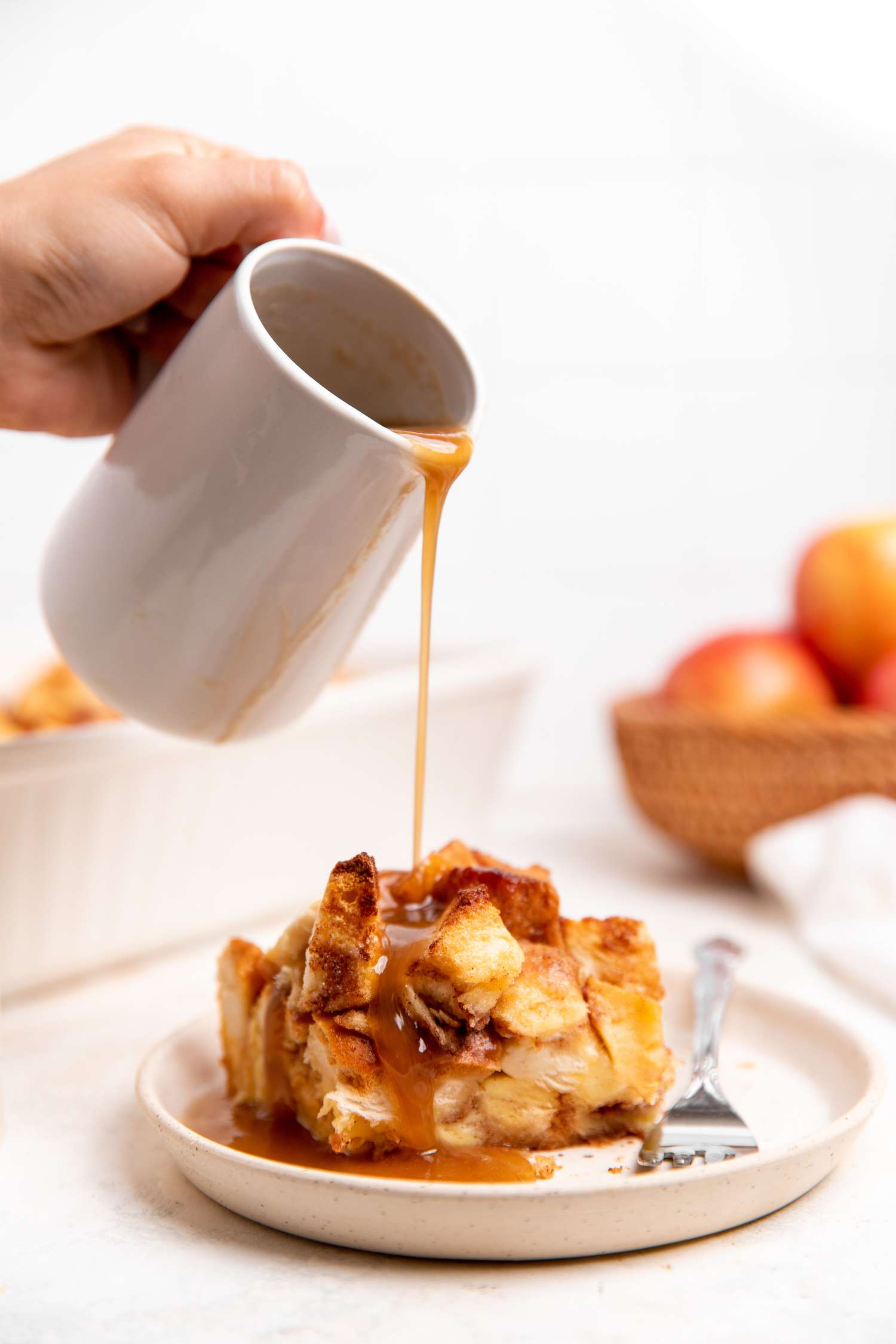 Slice 0f Apple Bread Pudding on a Plate with Sauce Drizzling from a Milk Pitcher