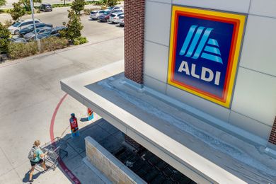 An Aldi store entrance with a shopper pushing a cart toward it