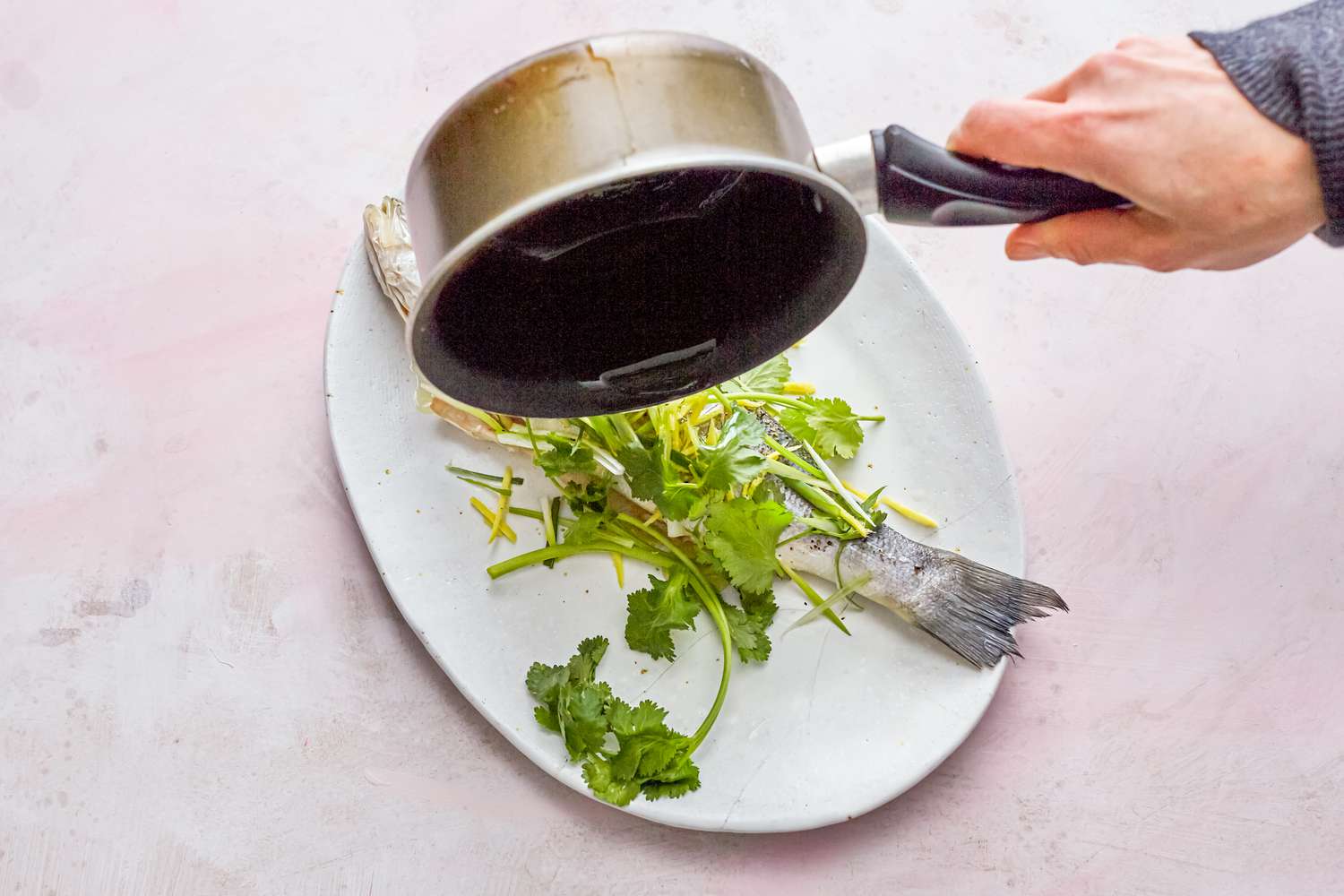 Pouring sauce over whole steamed fish with ginger and scallions
