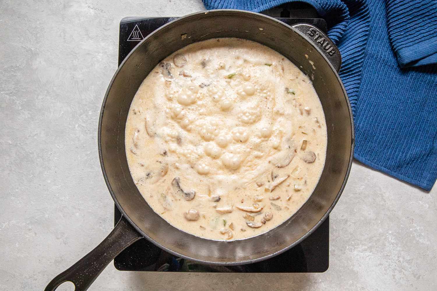 Heavy cream and chicken broth boiling in the cast iron skillet with the rest of the vegetables