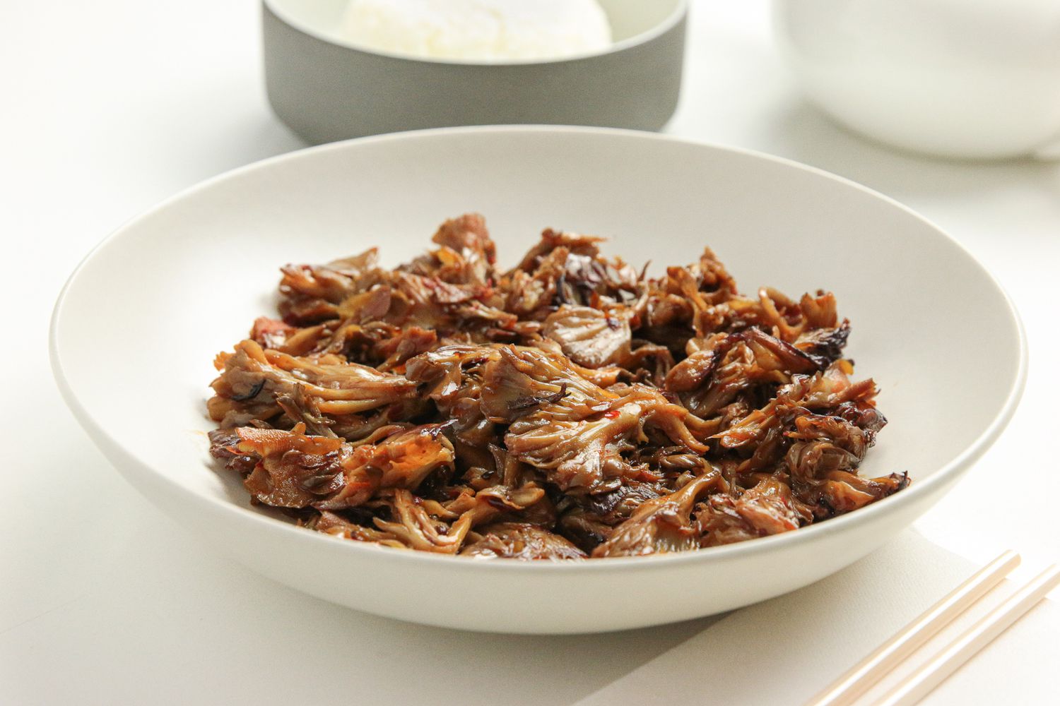 Stir-Fried Maitake Mushrooms with Garlic and Chile Oil in a Plate Next to a Pair of Chopsticks, a Bowl of Rice, and a Tea Kettle