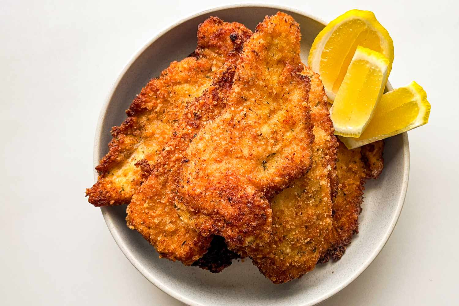Breaded chicken cutlets served on a plate with lemon wedges