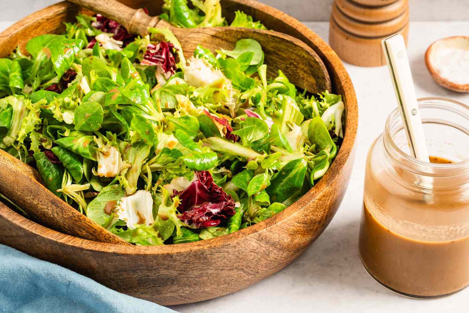 A wooden bowl with a mixed green salad beside a jar containing maple balsamic dressing