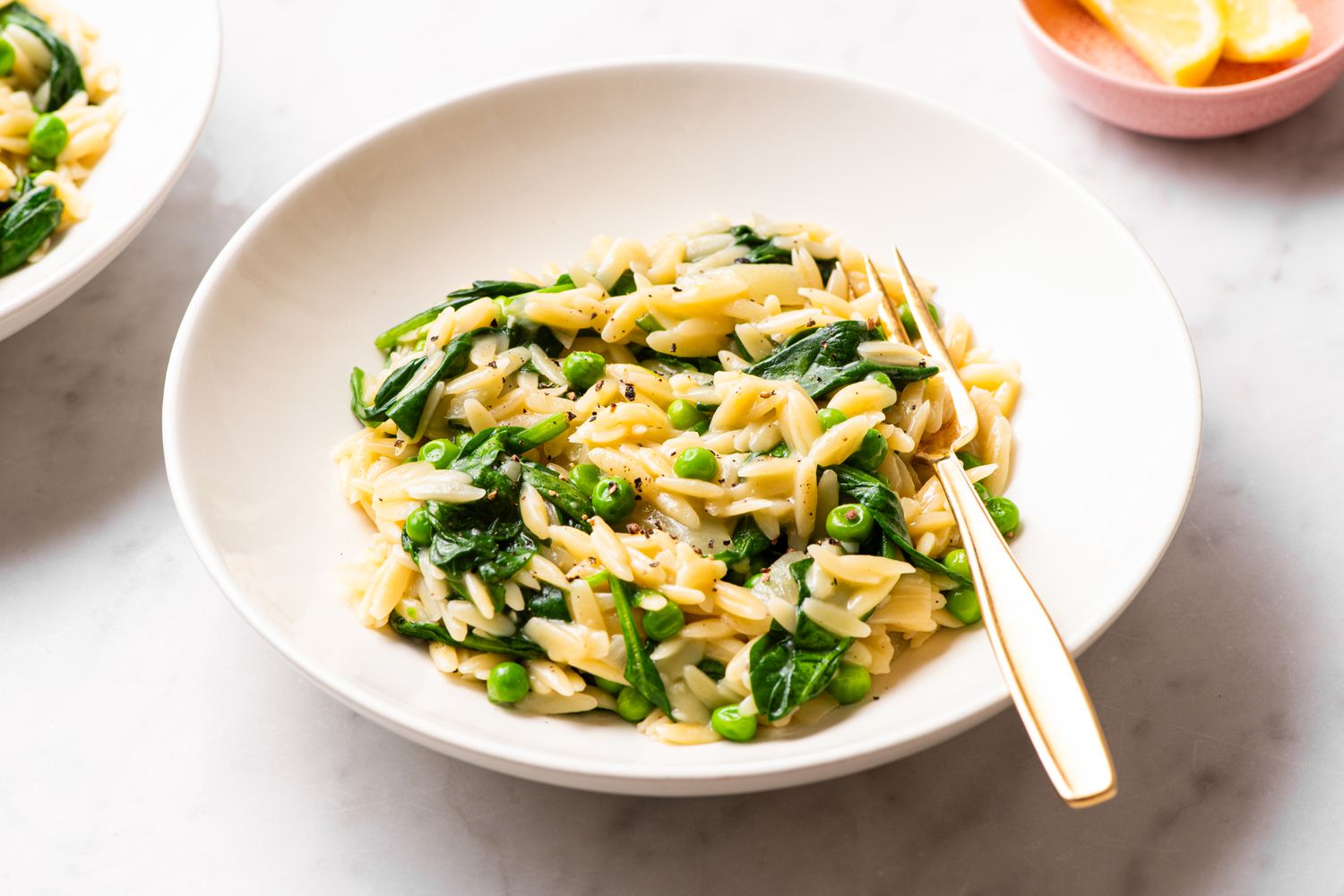 Dish of orzo pasta with spinach and peas, garnished and served in a white bowl