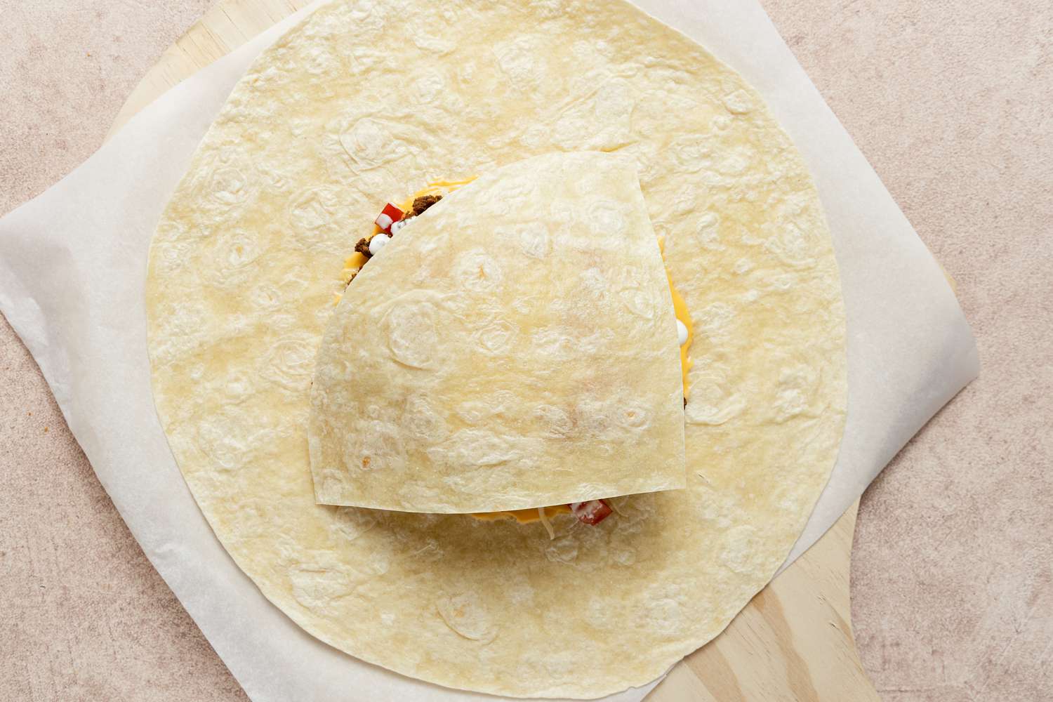 Tortilla Quarter Added to Stack of Ingredients for Homemade Crunchwrap Supreme Recipe