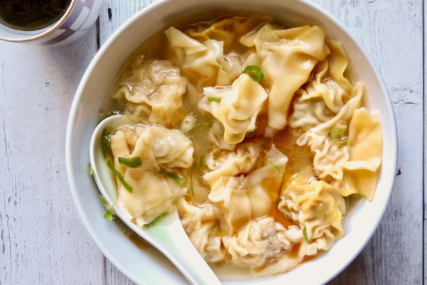 Overhead view of a bowl of pork and ginger wontons in chicken soup.