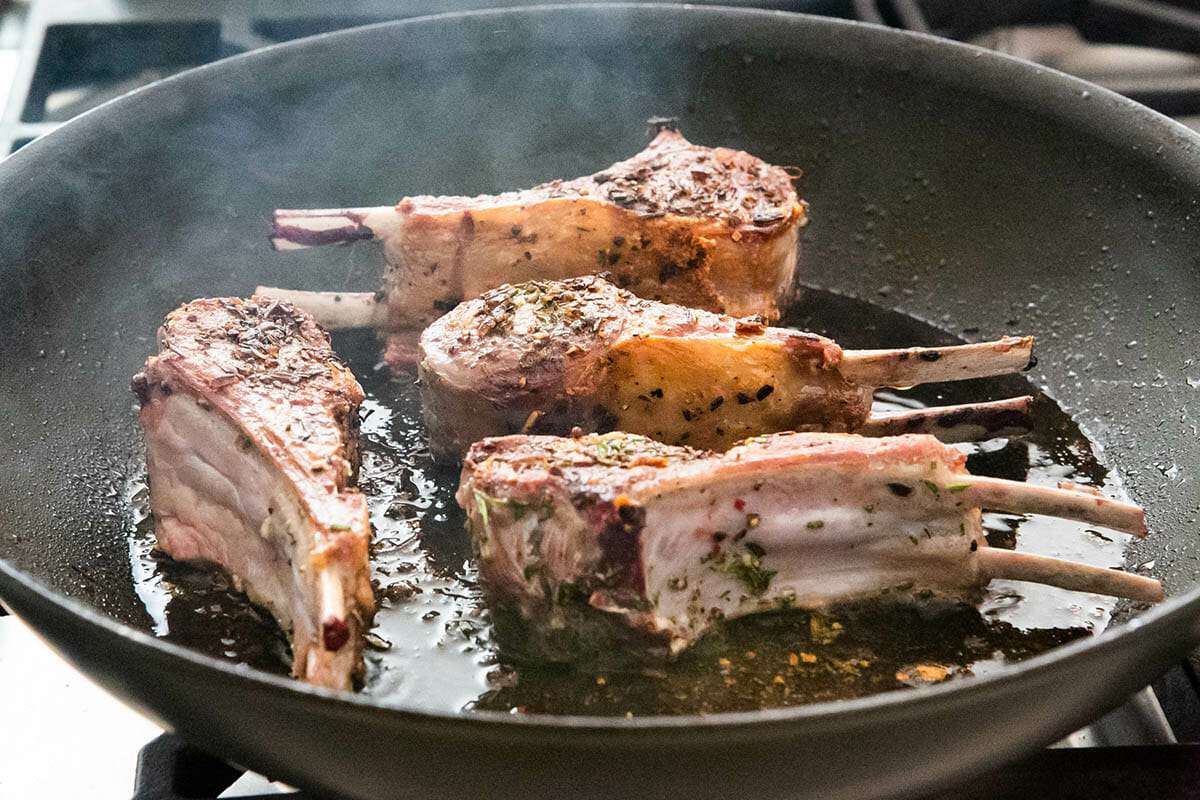 Four double rib lamb chops with rosemary and garlic, searing in a skillet