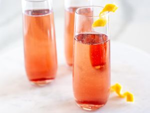 Three glasses of sparkling pink beverage garnished with orange peels served on a light marble surface